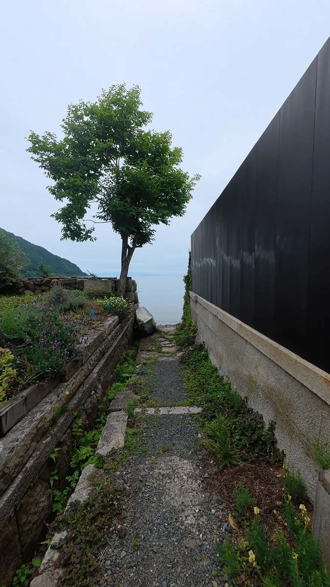 （左）蔵の脇の小道。抜けた先が湖岸です／（右）石積みの上に伏せられた小舟と、琵琶湖。対岸の山まで見えます