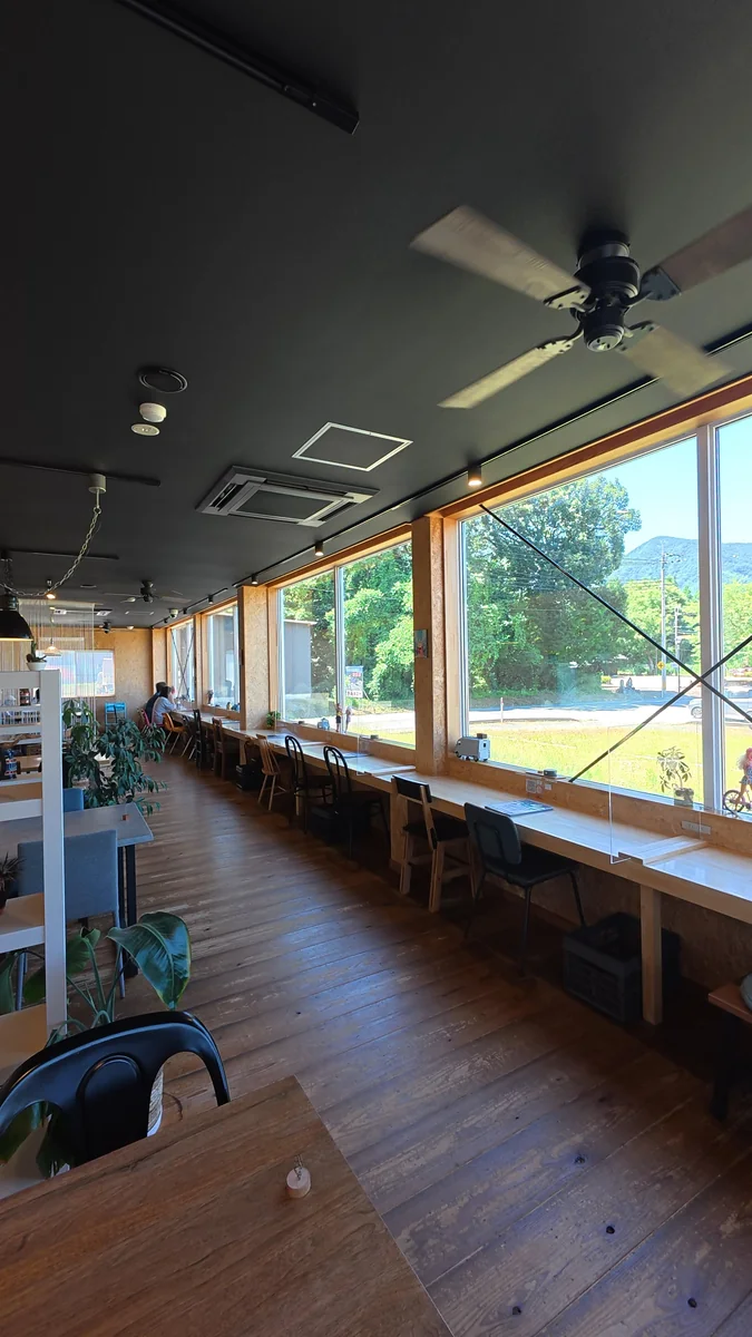 窓に面したカウンター席。外は並木道と山の緑(左)/土間に置かれた大きなソファ席(右)